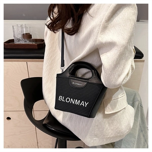 Detalle de bolso tipo cubo de paja negra con logo BLONMAY y correa ajustable al hombro