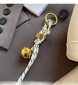 Close-up of black and white braided rope keychain with gold bell on a gray fabric