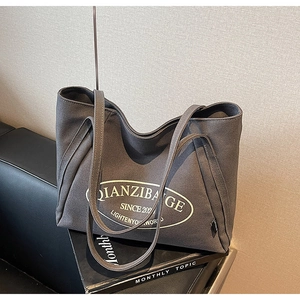 Detalle del bolso tote de lona gris oscuro con logo sobre sofá de cuero negro