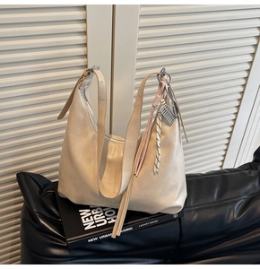 Detail of off-white hobo bag with pleated texture and decorative woven cord charm