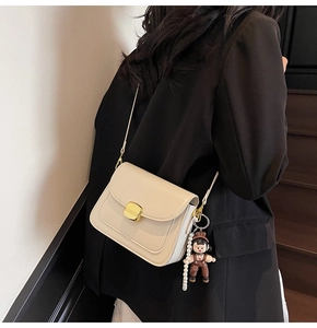Close-up of off-white minimalist crossbody bag with gold buckle and pearl charm accessory