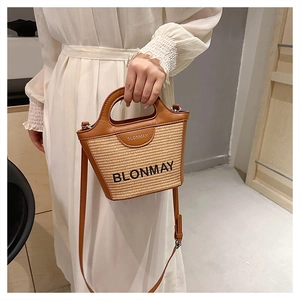 Detalle del bolso tipo cubo de paja BLONMAY con textura tejida y correa de cuero marrón