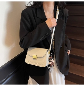 Close-up of cream PU leather crossbody bag with gold buckle and pearl doll charm