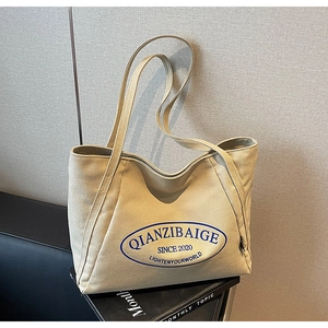 Primer plano detallado de un gran bolso tote de lona beige con logo azul y correas