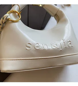 Close-up of beige dumpling bag with sen&jia logo embossing and gold ring detail