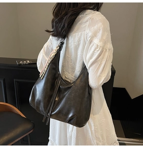 Detailed view of black pleated hobo bag featuring decorative silk scarf and leather tassels