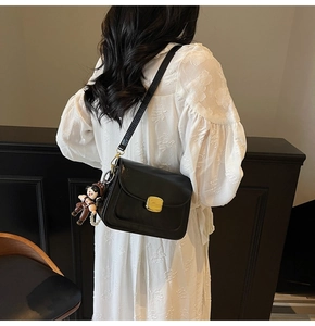 Detail of black crossbody square bag with gold buckle and pilot charm on model