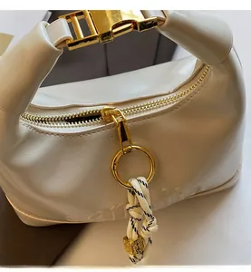 Close-up of smooth zipper with golden ring puller and woven rope on white leather bag
