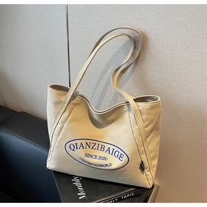 Detalle del bolso tote de lona beige con logo azul sobre superficie de cuero