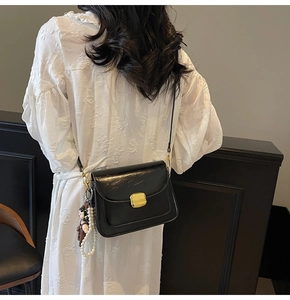 Detail of black crossbody bag with gold lock, pearl chain, and doll charm on model