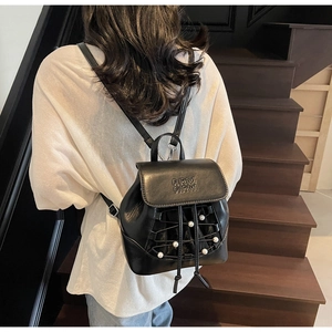 Detail of mini black leather backpack featuring embossed lettering and pearl cross-lacing