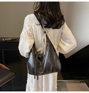 Detail of large black hobo bag with tassel and decorative checkered strap on shoulder