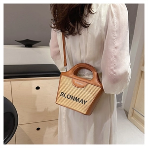 Detalle de un bolso cubo de paja trenzada con ribete de cuero marrón y bandolera