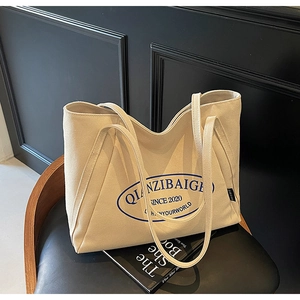 Detalle del bolso tote de lona crema con letras azules sobre una silla vintage