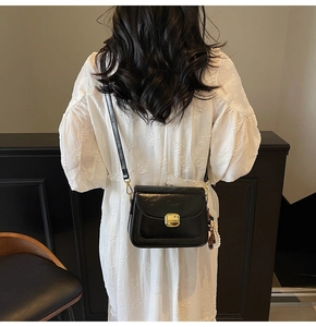 Detail of black glossy leather crossbody bag with gold lock and pearl bear charm