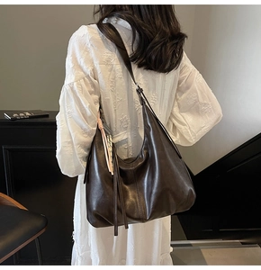 Detail of dark brown glossy leather Hobo bag with stylish side tassels on a model