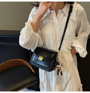 Detail of black leather crossbody bag with golden lock, pearl chain and cute charm