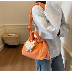 Detail of bright orange quilted bucket bag with drawstring closure and plush pendant