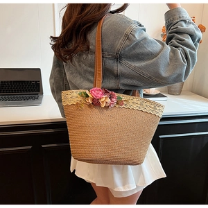 Detail of straw tote bag with lace trim and pink floral accents on leather shoulder strap