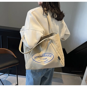 Primer plano del bolso tote de lona crema con letras azules llevado al hombro