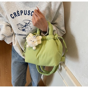 Detail of light green quilted bucket bag with drawstring and white plush cat charm