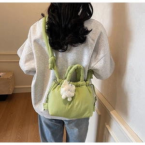 Rear view of a light green quilted bucket bag with drawstring and plush rabbit charm