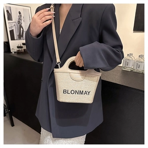 Detalle del bolso tipo cubo de paja tejida BLONMAY con ribete de cuero y bandolera