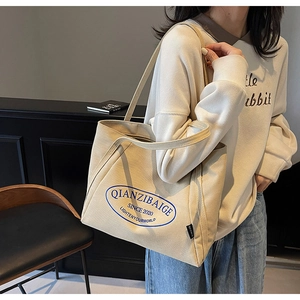 Detalle de un bolso tote grande de lona beige con logo azul mostrado por una modelo