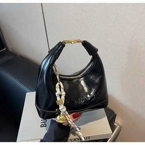 Detail of black glossy crescent bag with gold buckle handle and brand embossing