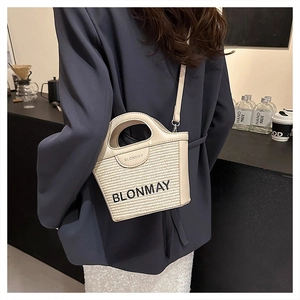 Detalle del bolso de paja trenzada crema con bordado de logo y asa de cuero
