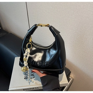 Detail of black glossy leather handbag with embossed logo and gold-tone hardware accents