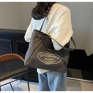 Detalle del bolso tote de lona gris oscuro con logo blanco llevado por una modelo