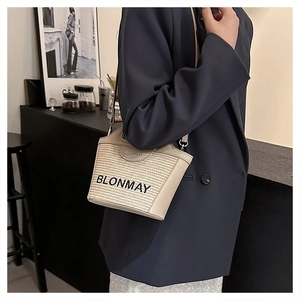 Detalle de un bolso tipo cubo de paja beige con ribete de cuero y logo BLONMAY bordado