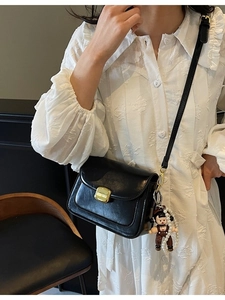 Elegant black leather crossbody bag with gold buckle and pearl doll charm detail