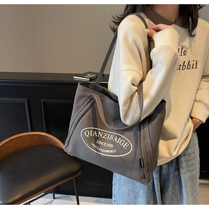Detalle del bolso tote de lona gris con letras blancas en modelo para perspectiva