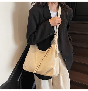 Detail of beige crescent shoulder bag with tassel and plaid bow on dark wood stairs