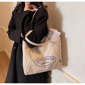 Bolso tote grande de lona beige con letras azules y revista en el interior