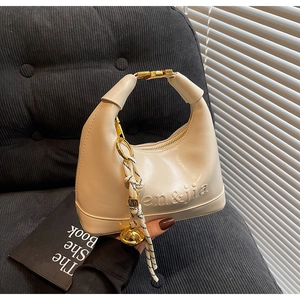 Detail of cream hobo bag featuring en&jia embossing and woven bell charm accent