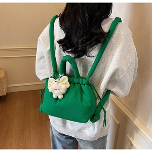 Detail of green quilted drawstring backpack with a plush monster charm on the side