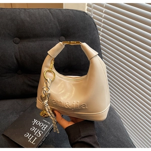 Detail of cream minimalist handbag with embossed logo and golden metal handle hardware