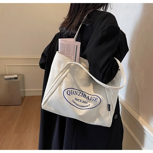 Detalle de bolsa tote de lona blanca con estampado de letras azules y bolsillo lateral