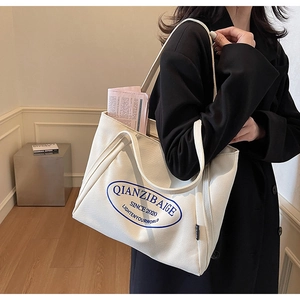Detalle de un gran bolso tote de lona beige con logo azul sobre un abrigo negro elegante