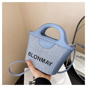 Detalle del bolso tipo cubo de cuero azul y tejido con correa larga y marca