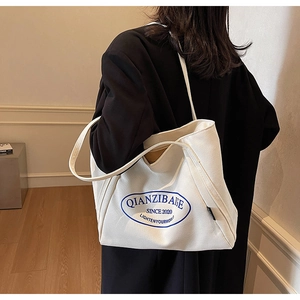 Detalle de bolso tote de lona blanca con estampado de logo azul y correa de hombro larga y cómoda