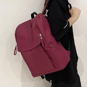 Détail du sac à dos en nylon bordeaux montrant la grande poche à rabat et le zip métallique