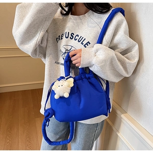 Detail of royal blue puffy bucket bag with drawstring closure and white plush charm