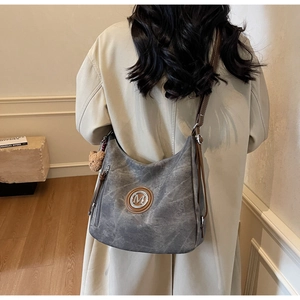 Dettaglio della borsa tote grigia con logo M e ciondolo a forma di orso indossata da modella