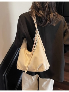 Large beige hobo bag with fringe and woven details on a model in a black blazer