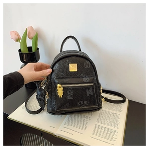 Close-up of black leather mini backpack with bear charms and gold logo on a book