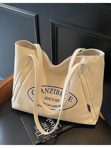 Bolso tote grande de lona beige con estampado azul sobre silla de madera negra